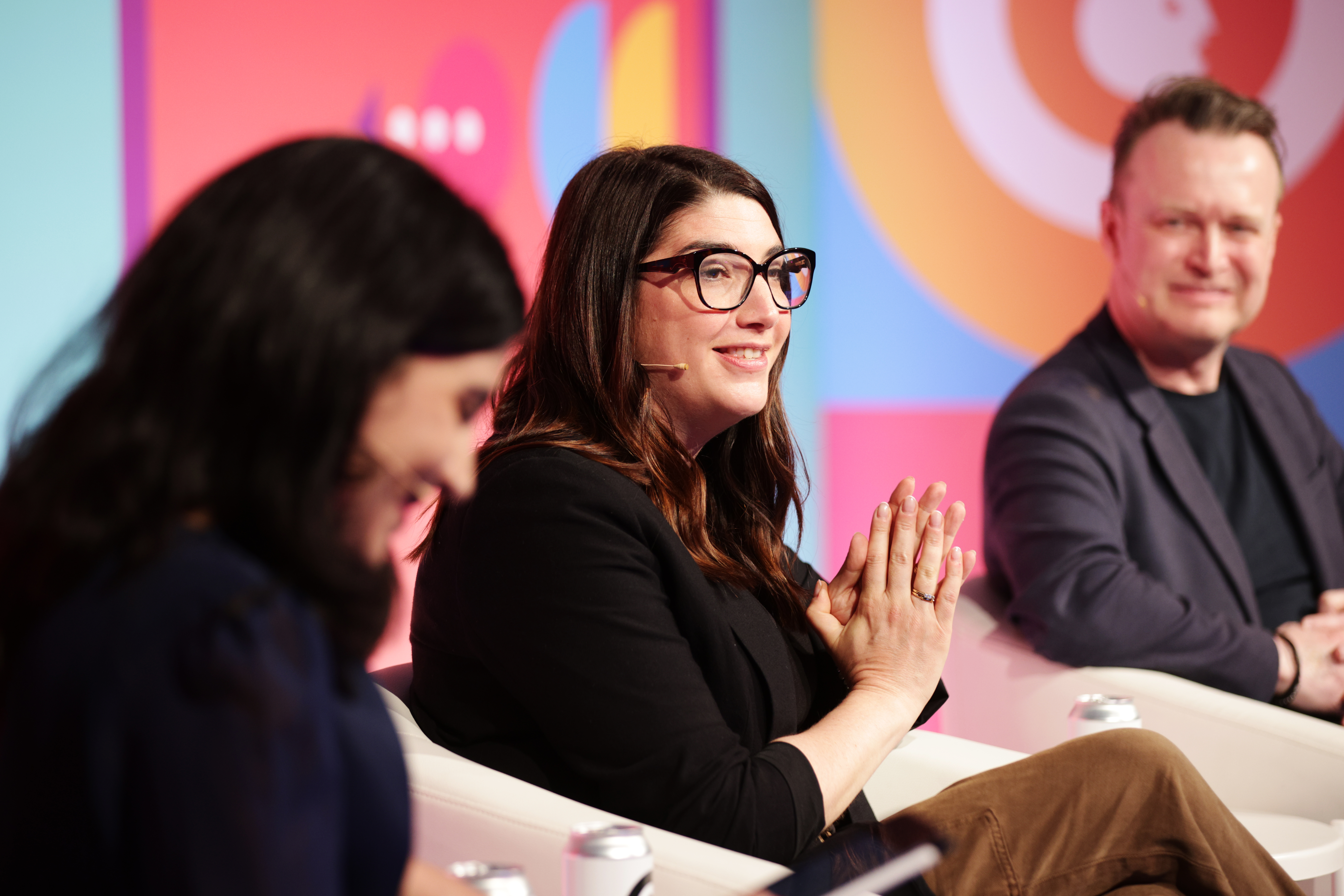 Jane Stiller mid speech on a cream chair holdin gher hands togetehr. She has mid-long brown hair, black glasses and a black three quarter length sleeve top.