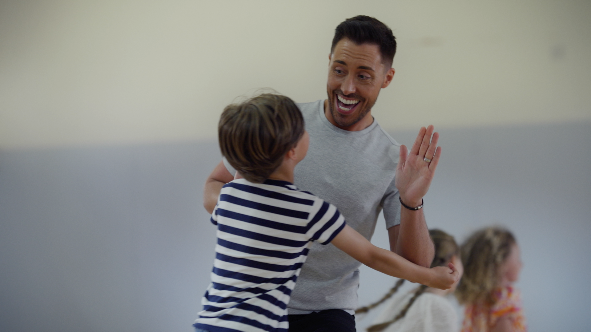 Film actor Ross Adams high fives a leaping child in a black and white striped shirt.