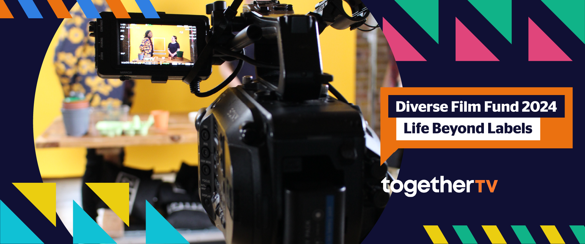 Orange speech bubble with text "Diverse Film Fund 2024: Life Beyond Labels". Behind the speech bubble is a graphic with colourful geometric shapes and a film camera shooting a set with two people in front of a yellow backdrop