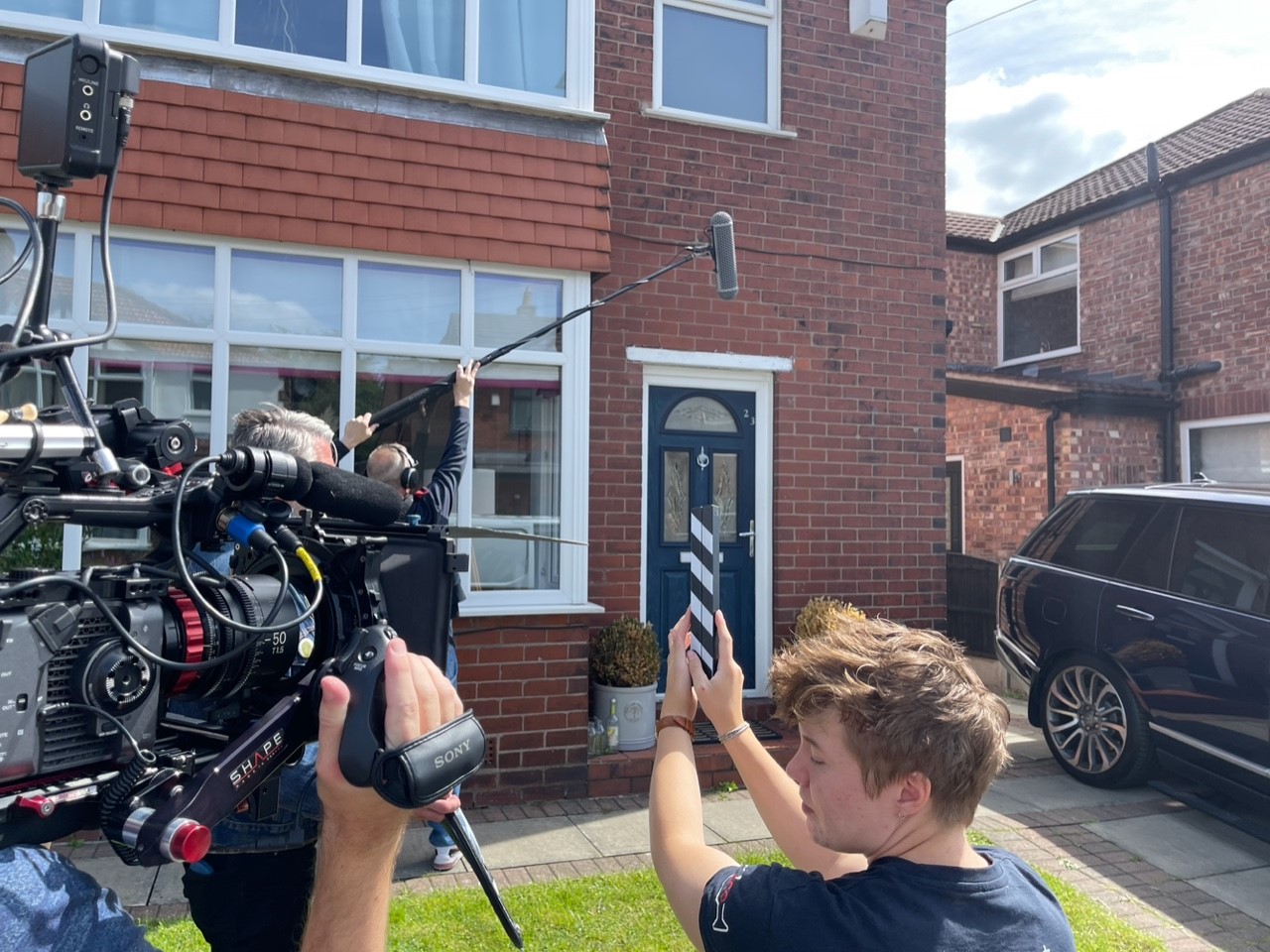 The film crew stands outside a contributor's house preparing to film.