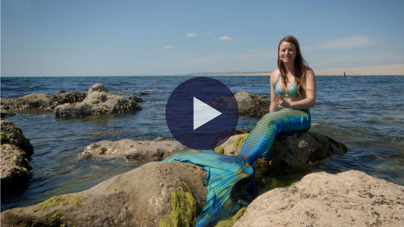 Still from Mermaids Really Do Exist where mermaid Catriona is wearing her turquoise mermaid tail and sitting on a rock in the sea